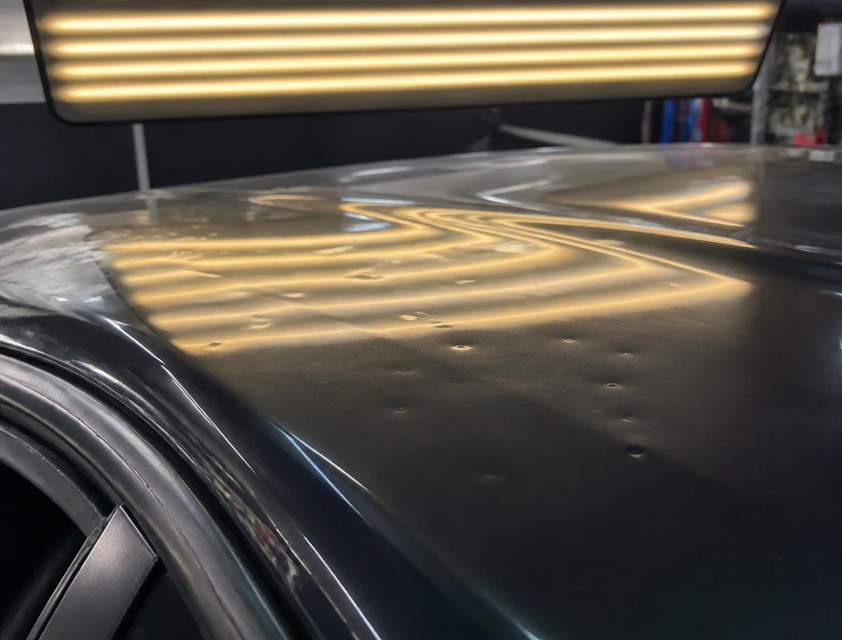 Hail dents on a car roof revealed under striped LED inspection light